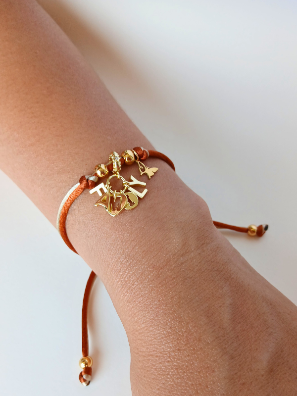 Pulsera ajustable hilo satinado con dije family con baño de oro.