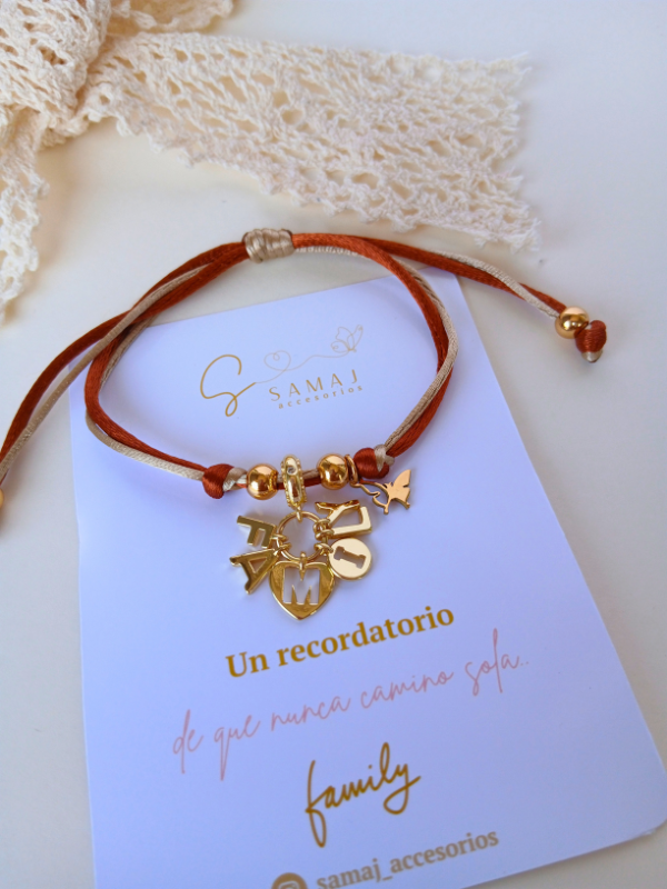 Pulsera ajustable hilo satinado con dije family con baño de oro.