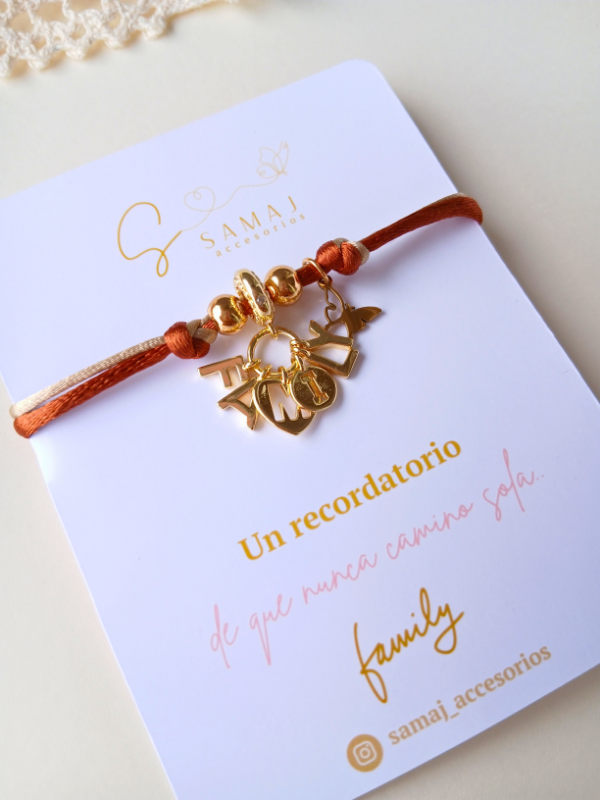 Pulsera ajustable hilo satinado con dije family con baño de oro.
